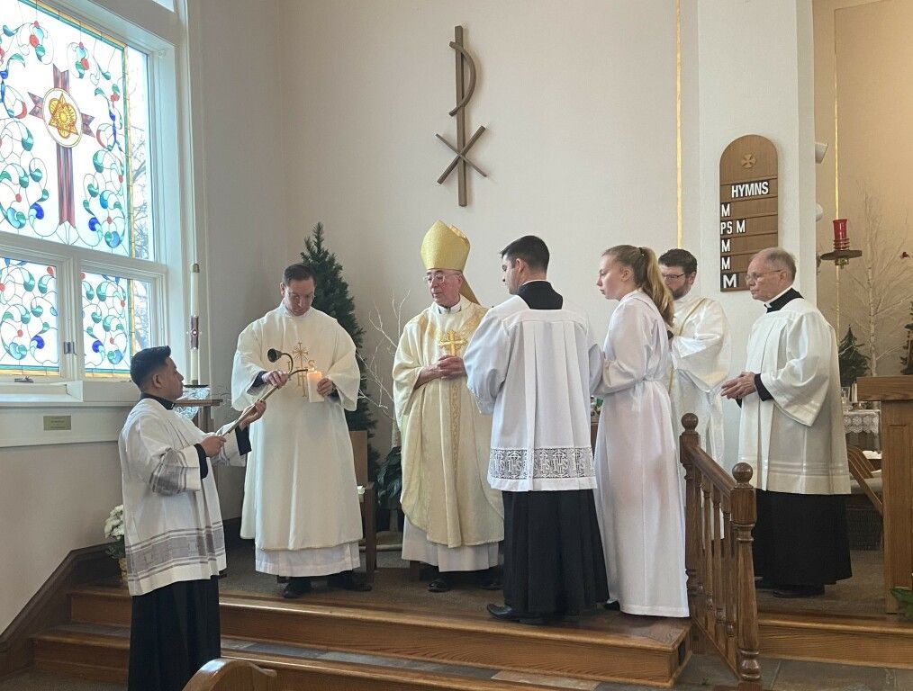 Clergy in white robes gathered on a church stage during a religious ceremony