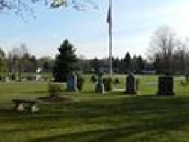 Grassy park with a flagpole, picnic table, and small stone monuments under a clear sky