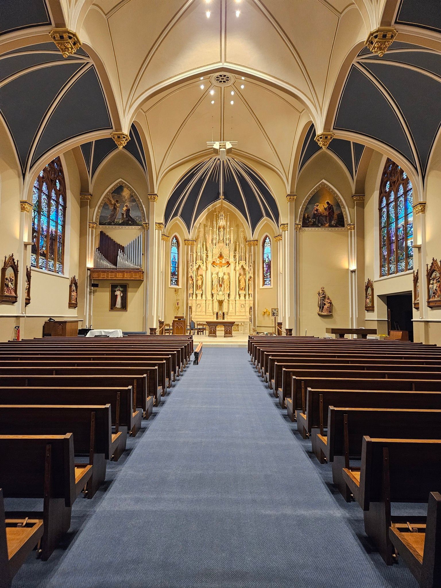 Interior of a Gothic church nave with pews, stained glass windows, and an ornate altar at the far end