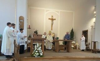 Catholic church altar with priests and altar servers during a service under a large crucifix
