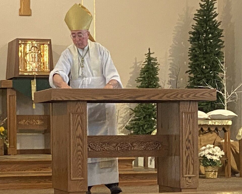 Priest in white vestments and gold mitre standing behind an altar in a church sanctuary