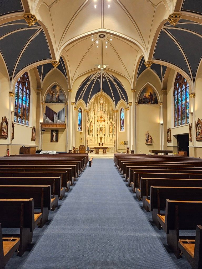 Empty church interior with blue carpet aisle, dark pews, and ornate gold altar at the front