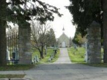 Tree-lined path leading to a distant church entrance, framed by stone gateposts
