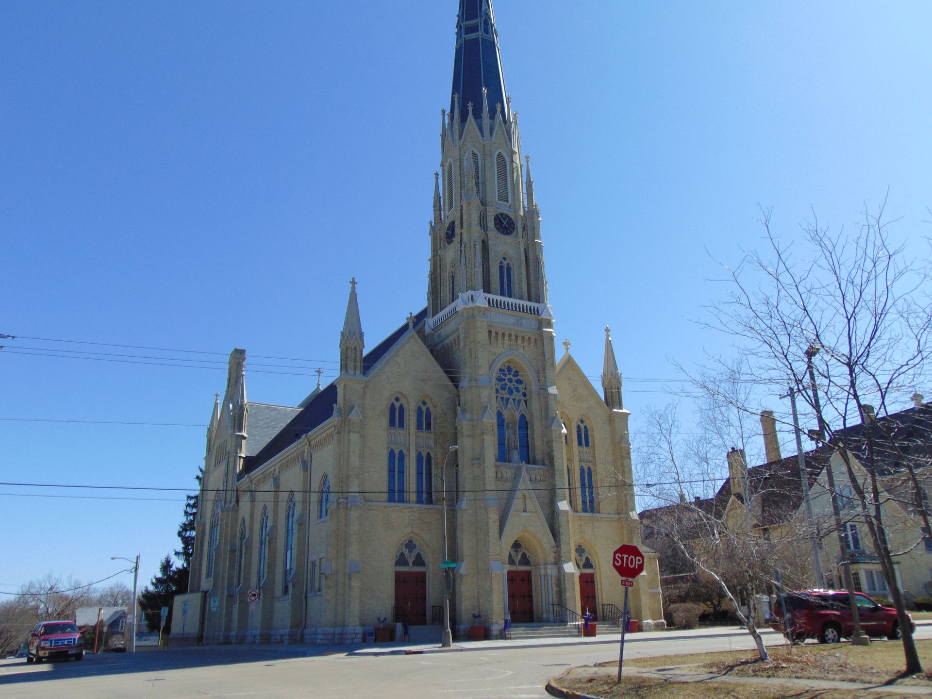 Gothic-style church with a tall spire on a sunny street corner under a clear blue sky