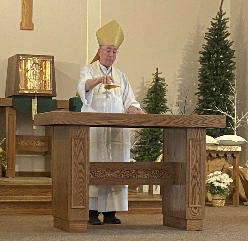 Priest in white vestments and yellow mitre holding a chalice at a church altar