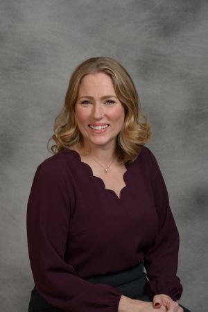 Smiling woman in a burgundy blouse posed against a gray studio backdrop