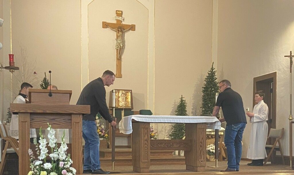 People arranging the altar in a church, with a crucifix and nativity scene visible.