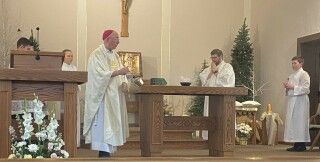 Priest and altar servers at a church altar during Mass, with candles and flowers in the background