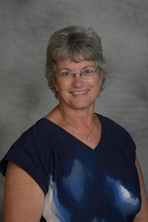 Smiling woman in glasses wearing a blue top against a gray backdrop