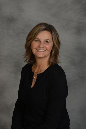 Smiling woman in a black top posed against a gray studio backdrop
