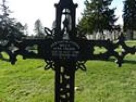 Decorative black iron grave cross in a grassy cemetery with trees in the background