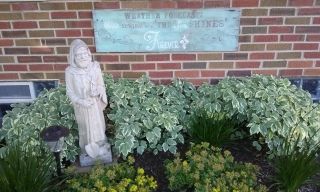 Garden statue beside shrubs in front of a brick wall with a weathered sign