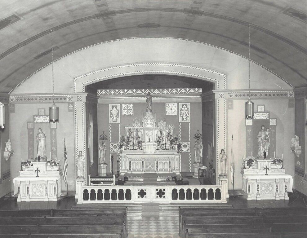 Ornate church altar with statues and candles beneath a large arched ceiling