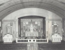 A church altar with candles and decorations beneath a large arched ceiling, viewed from the center aisle
