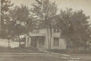 Old two-story house partially hidden by trees in a rural yard
