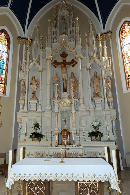 Church altar with crucifix, statues, and white lace-covered altar in a vaulted sanctuary