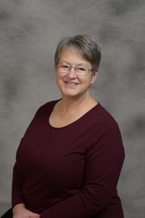 Portrait of a smiling person in a maroon top against a gray studio backdrop