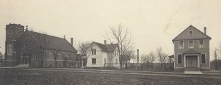 Historic sepia photo of three houses along a rural street, with bare trees and open ground.