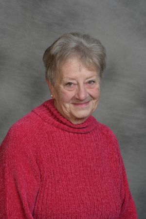 Smiling woman in a bright pink sweater against a gray studio backdrop
