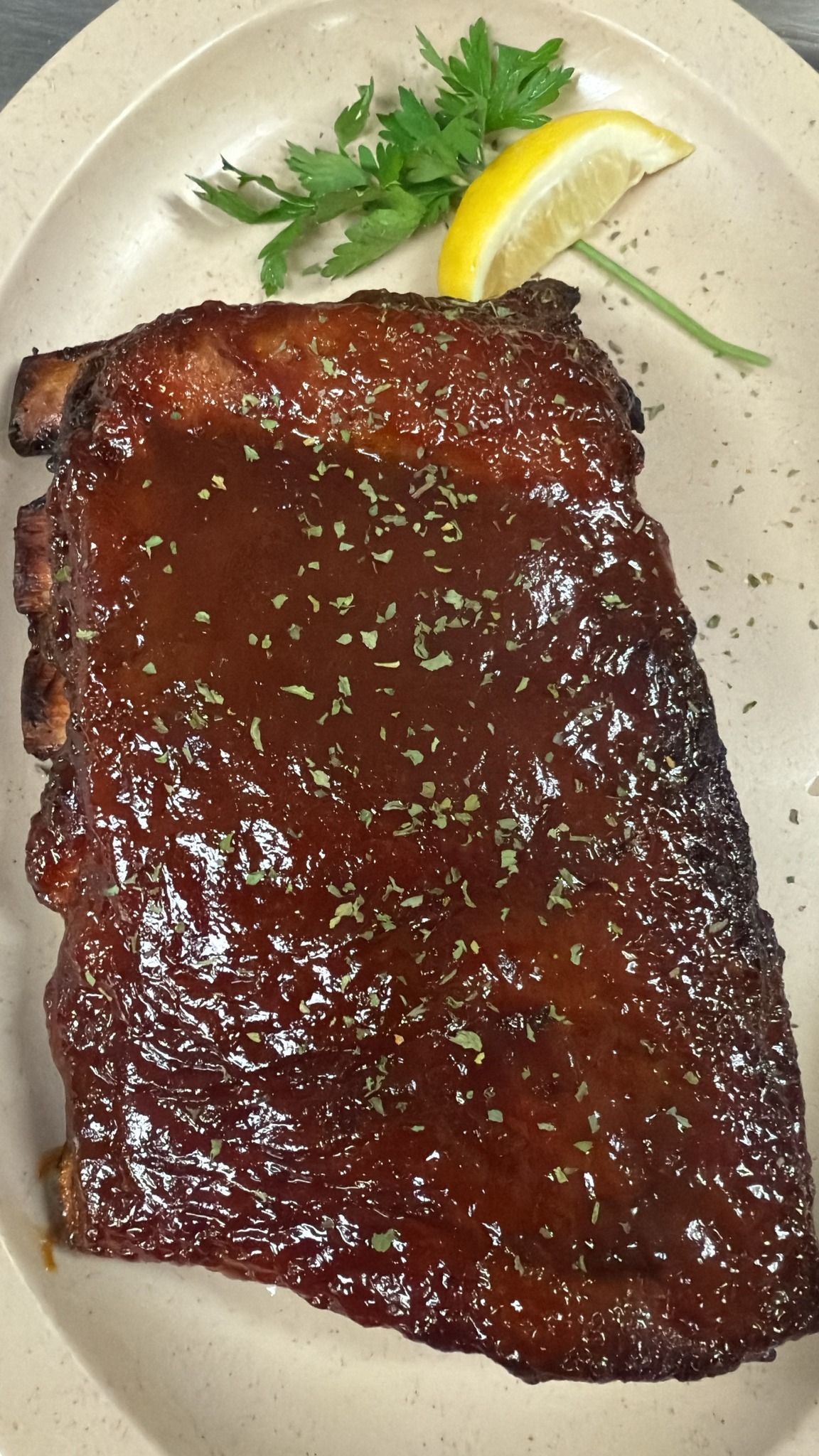 Rack of glazed ribs on a plate, garnished with parsley and lemon. At High Tide Harry's
