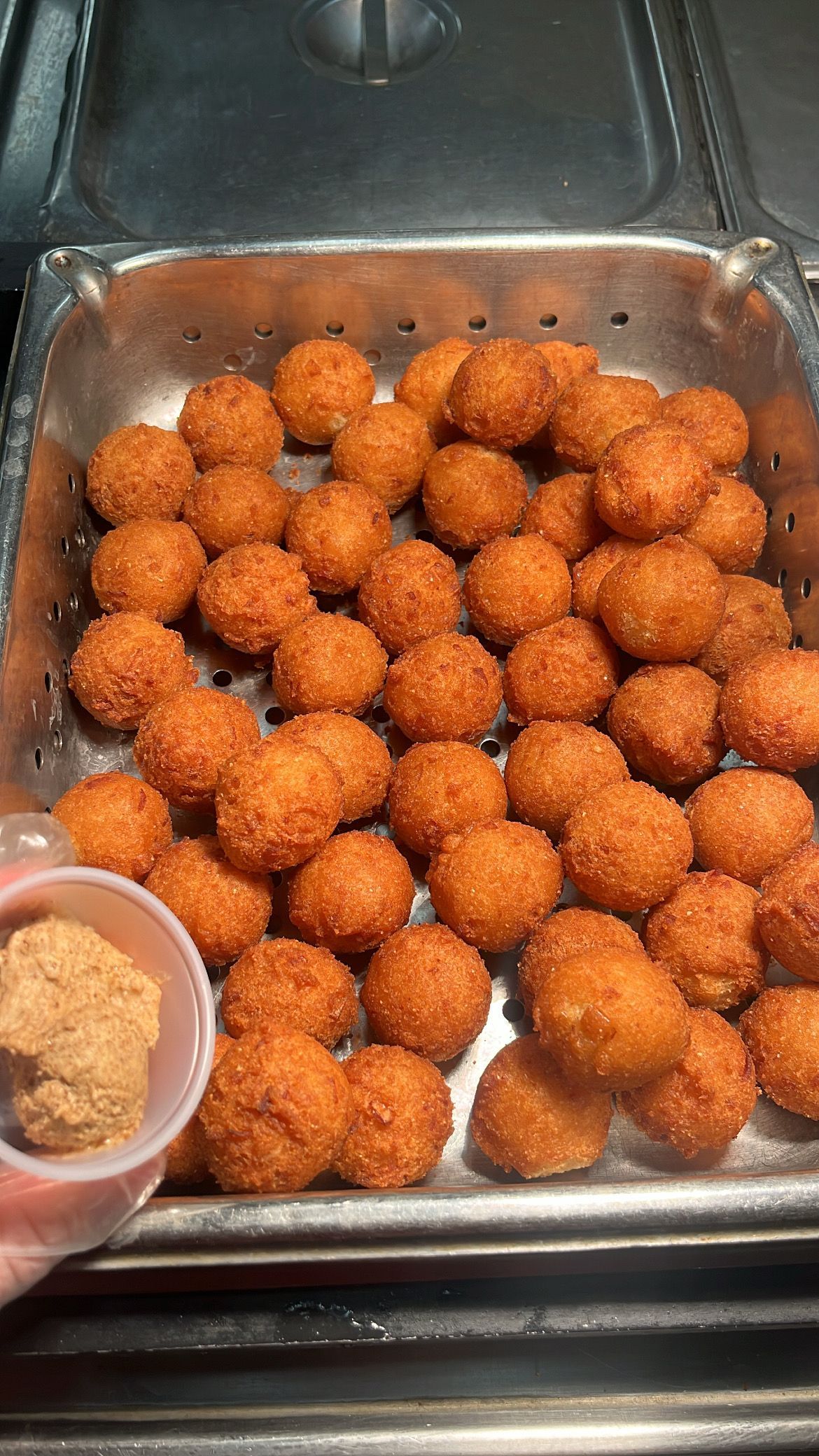 Golden-brown fried food balls in a metal basket with a small container of dipping sauce. At High Tide Harry's