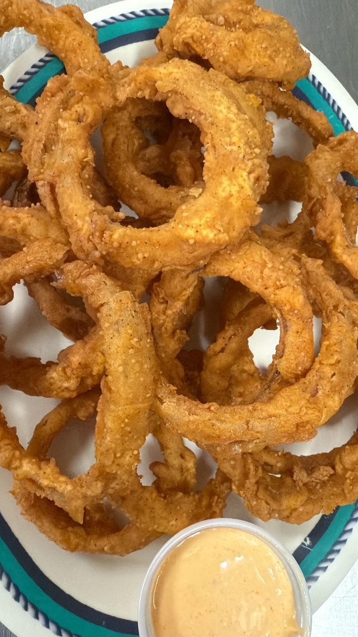 Plate of golden brown onion rings with dipping sauce. At High Tide Harry's