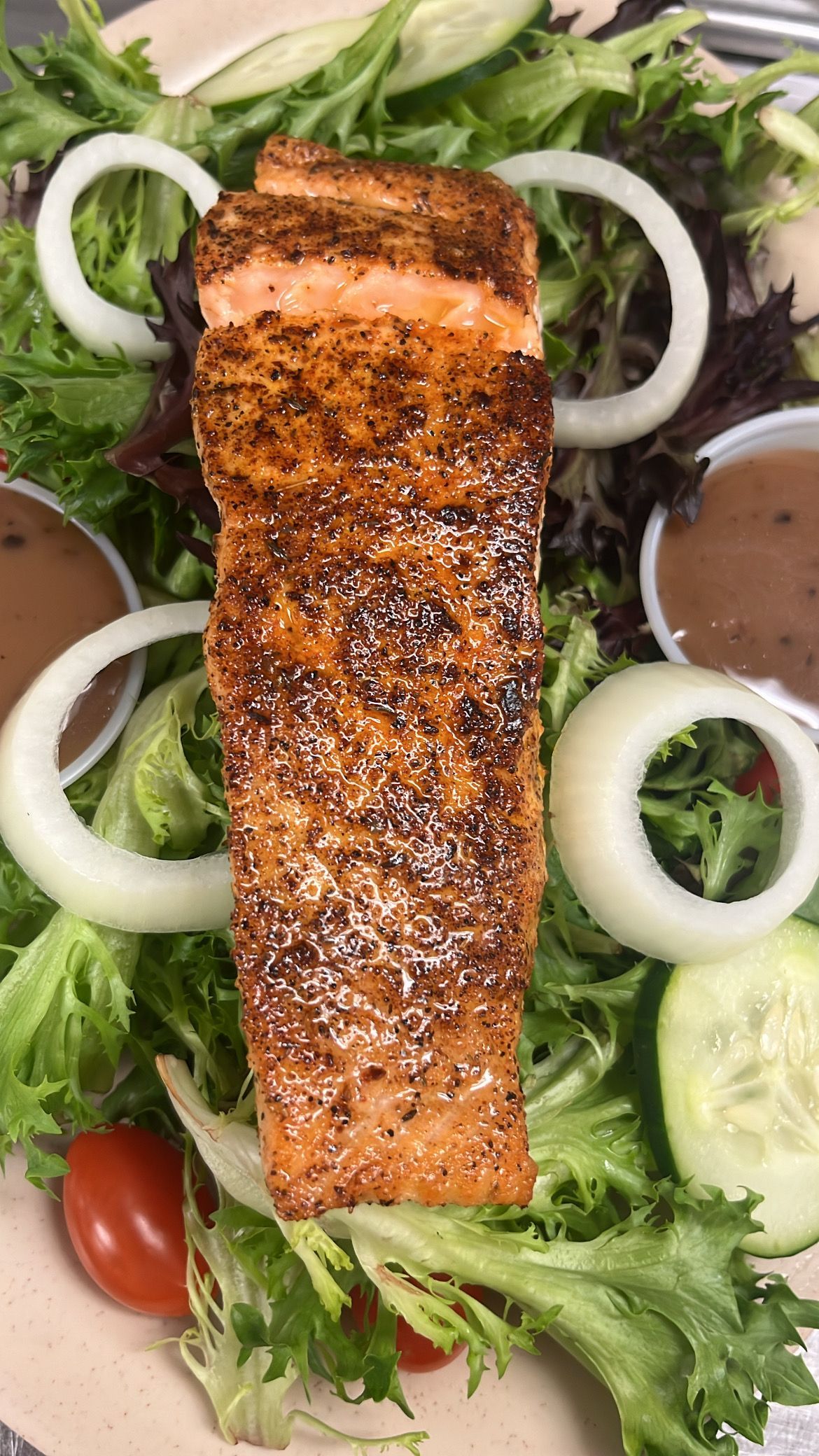 Salmon salad with mixed greens, onion rings, cherry tomatoes, cucumbers, and dressing in small cups. At High Tide Harry's