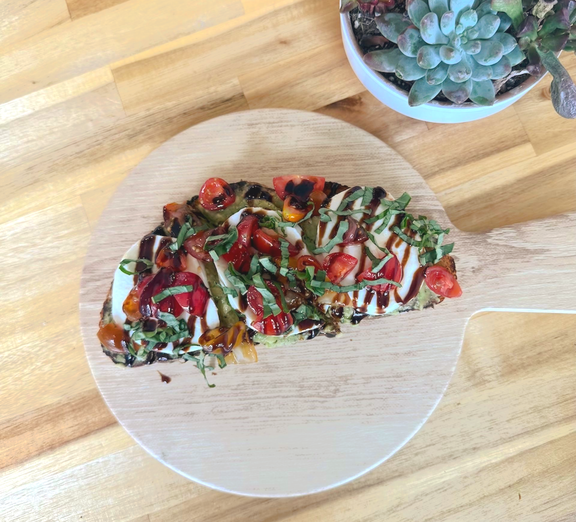Bruschetta on wooden board: toasted bread topped with mozzarella, tomatoes, and basil, with succulent plant in background.