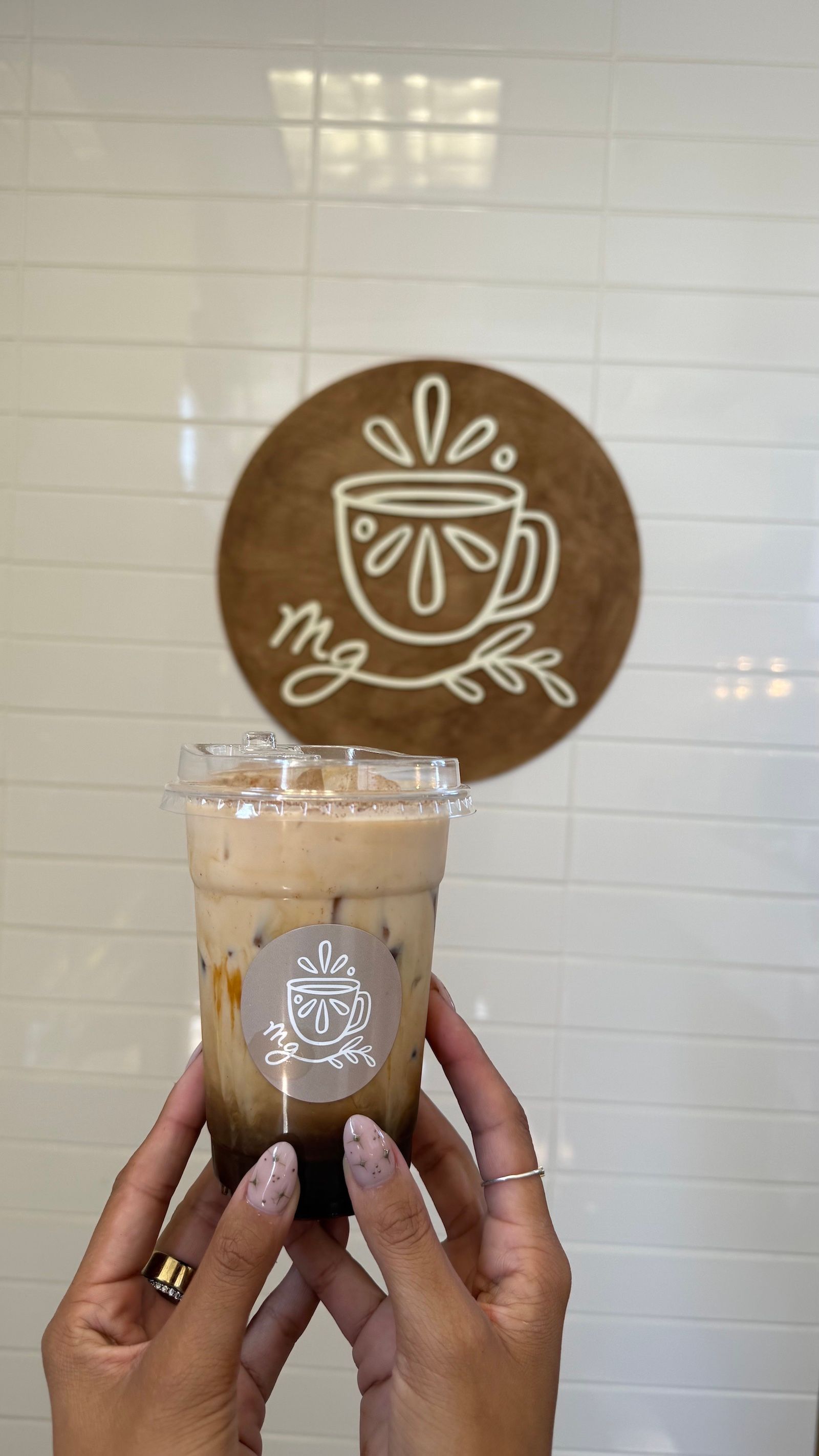 A hand holding an iced coffee drink with a logo in the background.