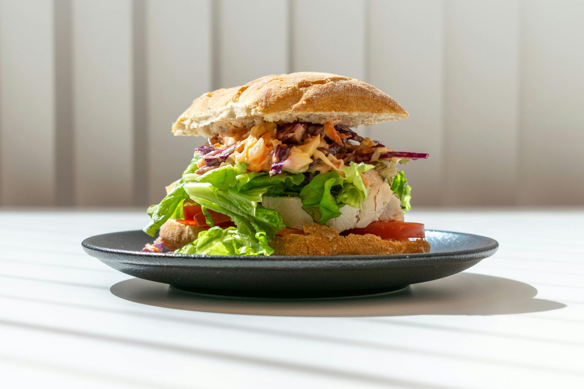 Sandwich with lettuce, tomato, and coleslaw on a black plate.