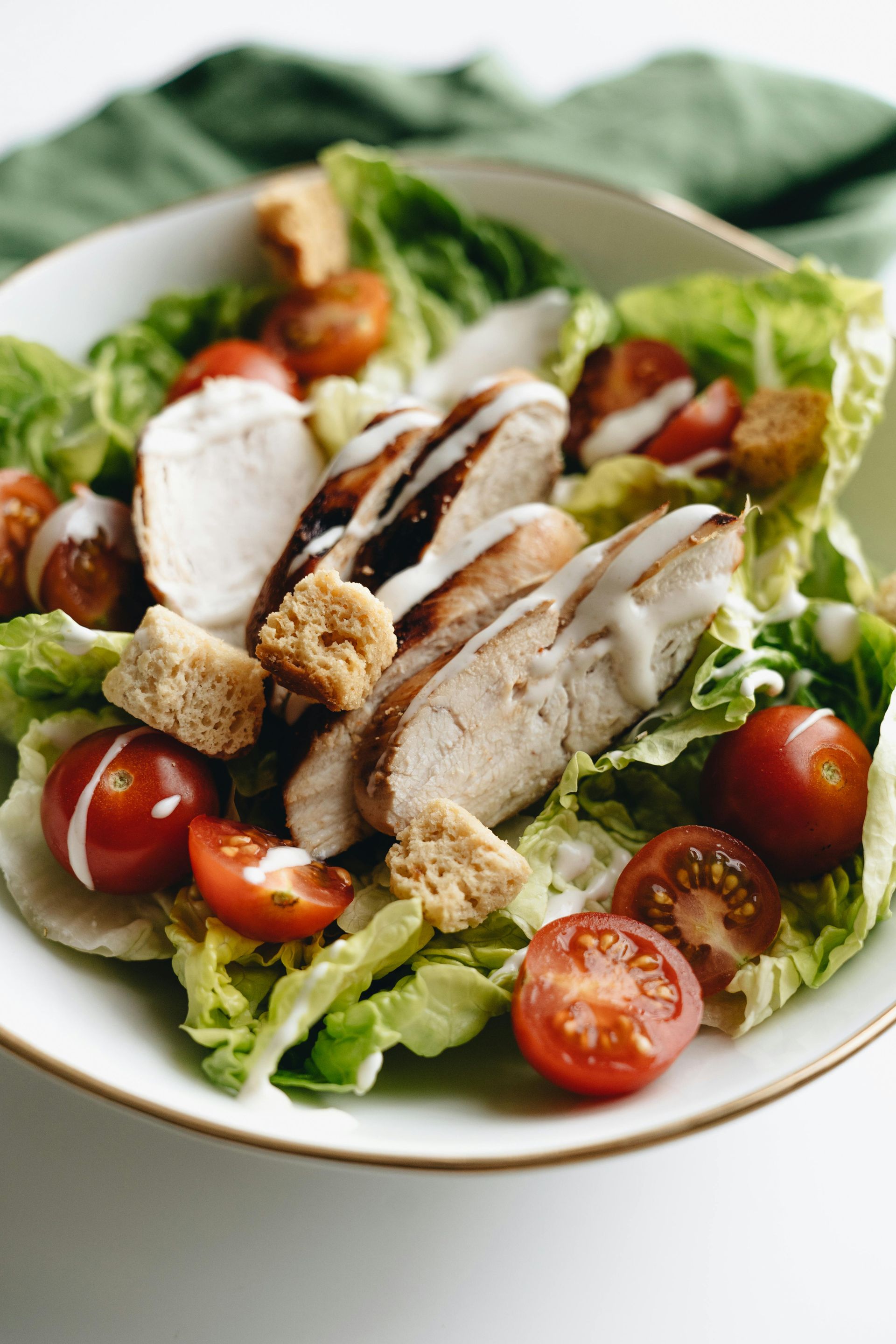 Chicken Caesar salad in a white bowl with croutons, tomatoes, and dressing.