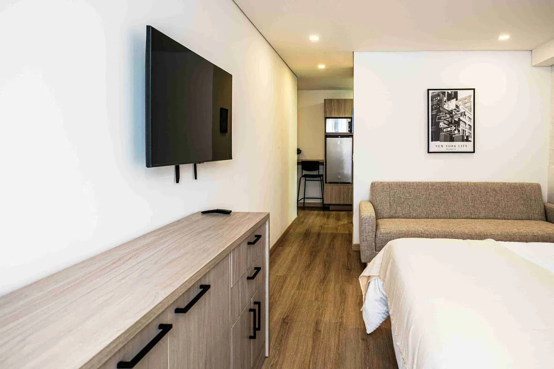 Vista interior de apartasuite Nova Iorque Bogotá. Un mueble de TV de madera, un sofá cama, un cuadro decorativo y parte de una cama