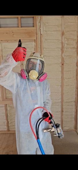 Person in protective suit spraying foam insulation on a wall.