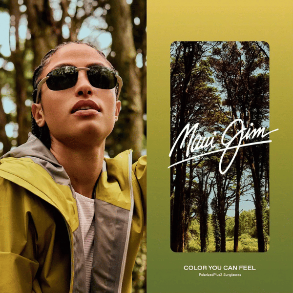 A woman wearing sunglasses and a yellow jacket is standing in the woods.