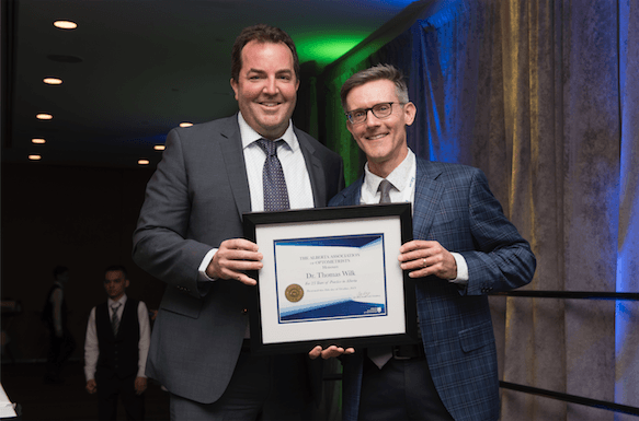 Two men in suits and ties are holding a framed certificate.