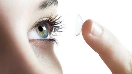 A woman is putting a contact lens in her eye.