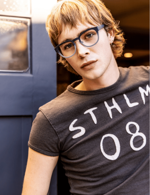 Person with glasses and tousled blond hair wearing a dark