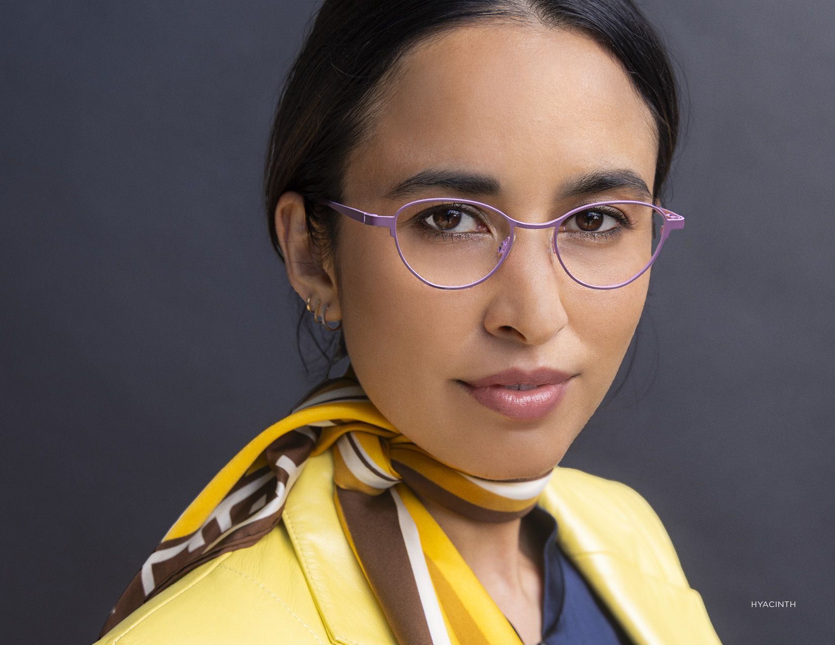 Portrait of a person wearing purple glasses and a yellow scarf against a dark background