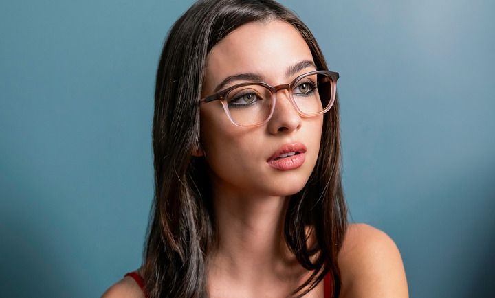 A woman wearing glasses is standing in front of a blue wall.