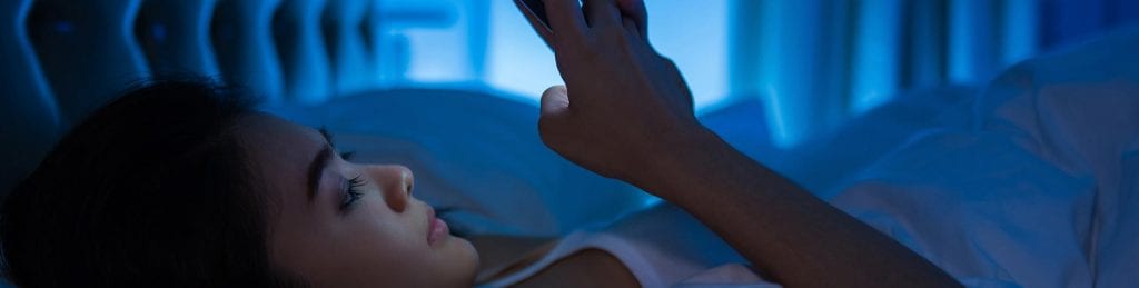 A woman is laying in bed looking at her cell phone.
