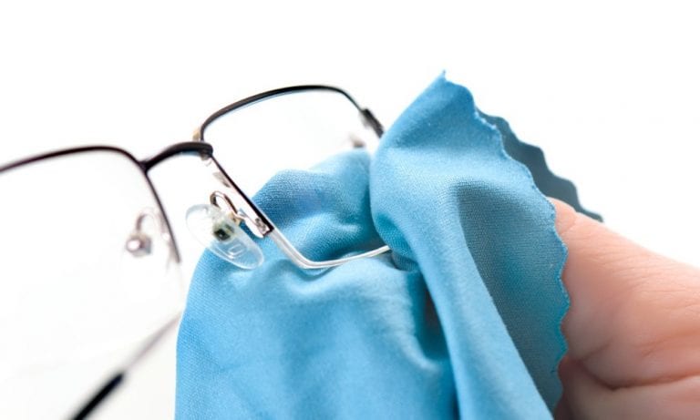 A person is cleaning a pair of glasses with a blue cloth.