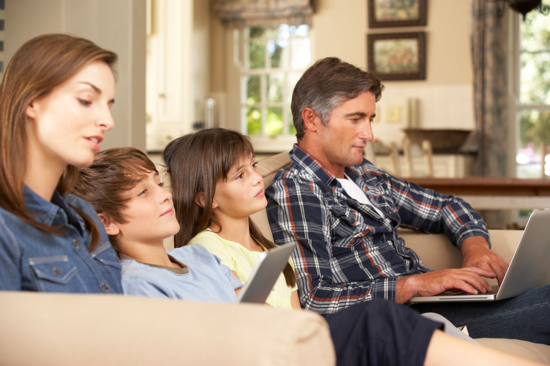 A family is sitting on a couch using laptops.
