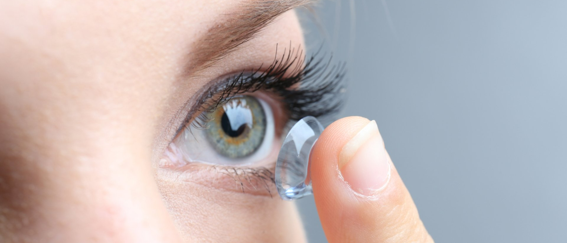 A woman is putting a contact lens in her eye.
