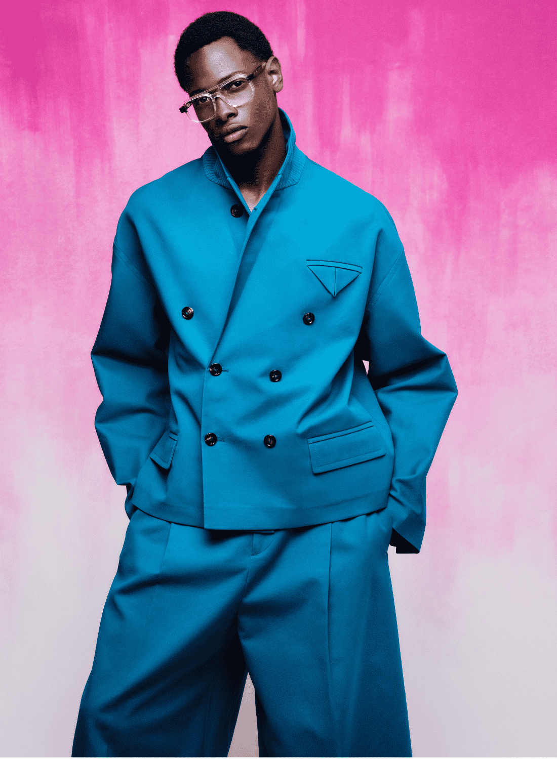 Person in a turquoise suit posing against a pink backdrop