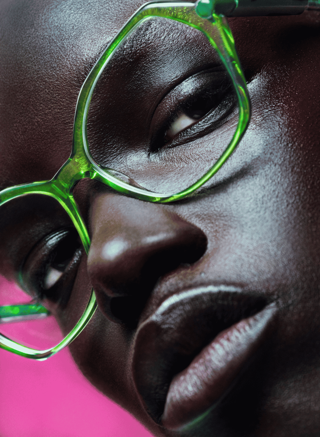 Close-up of a person wearing bright green glasses against a pink background