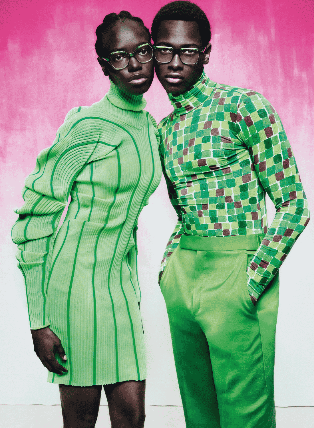 Two models in bright green outfits posing against a pink backdrop