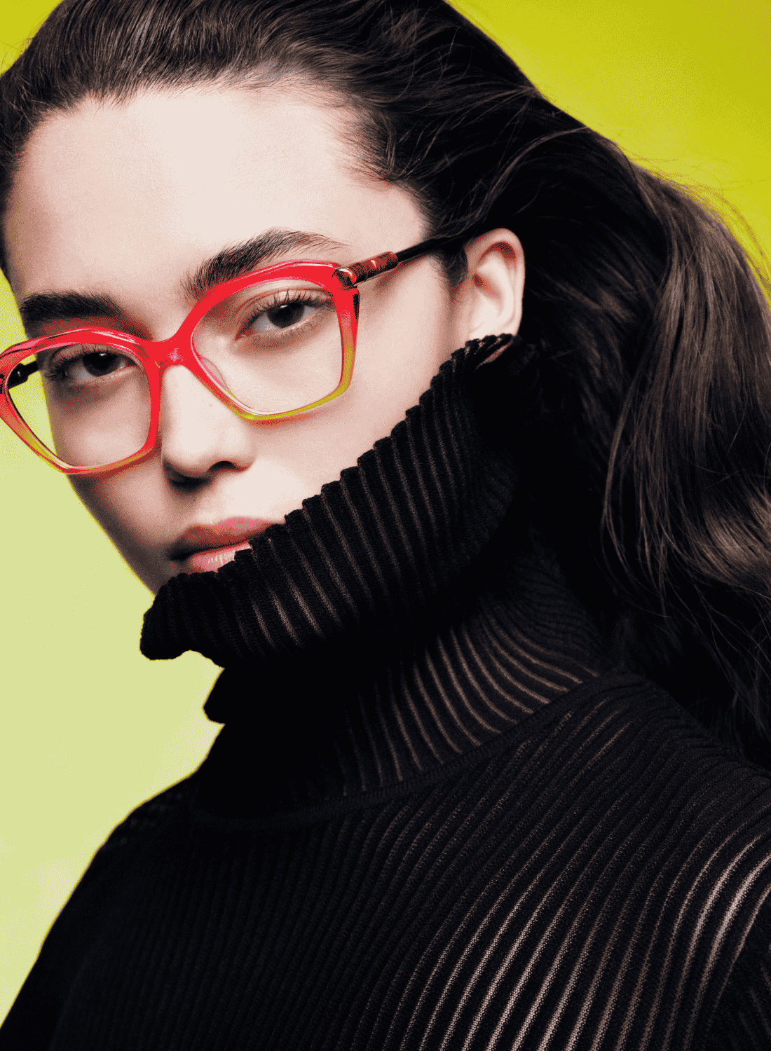 Person in red glasses and a black ribbed turtleneck against a bright yellow background.