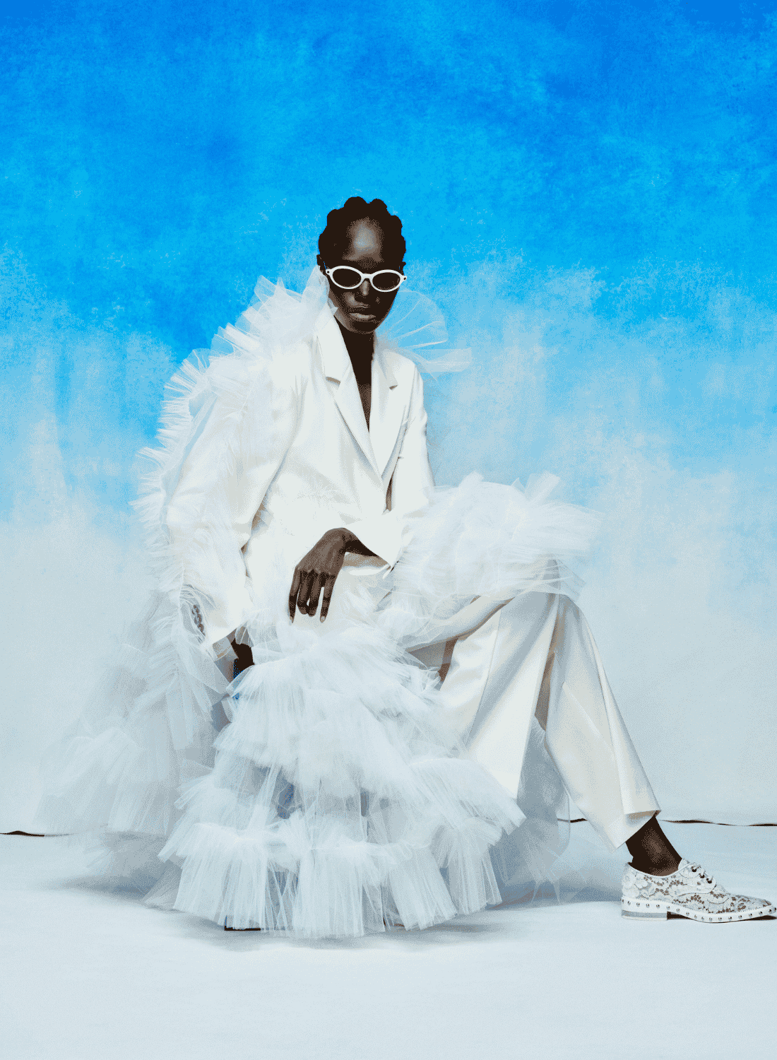 Person in a white suit and tulle skirt posing against a bright blue background.