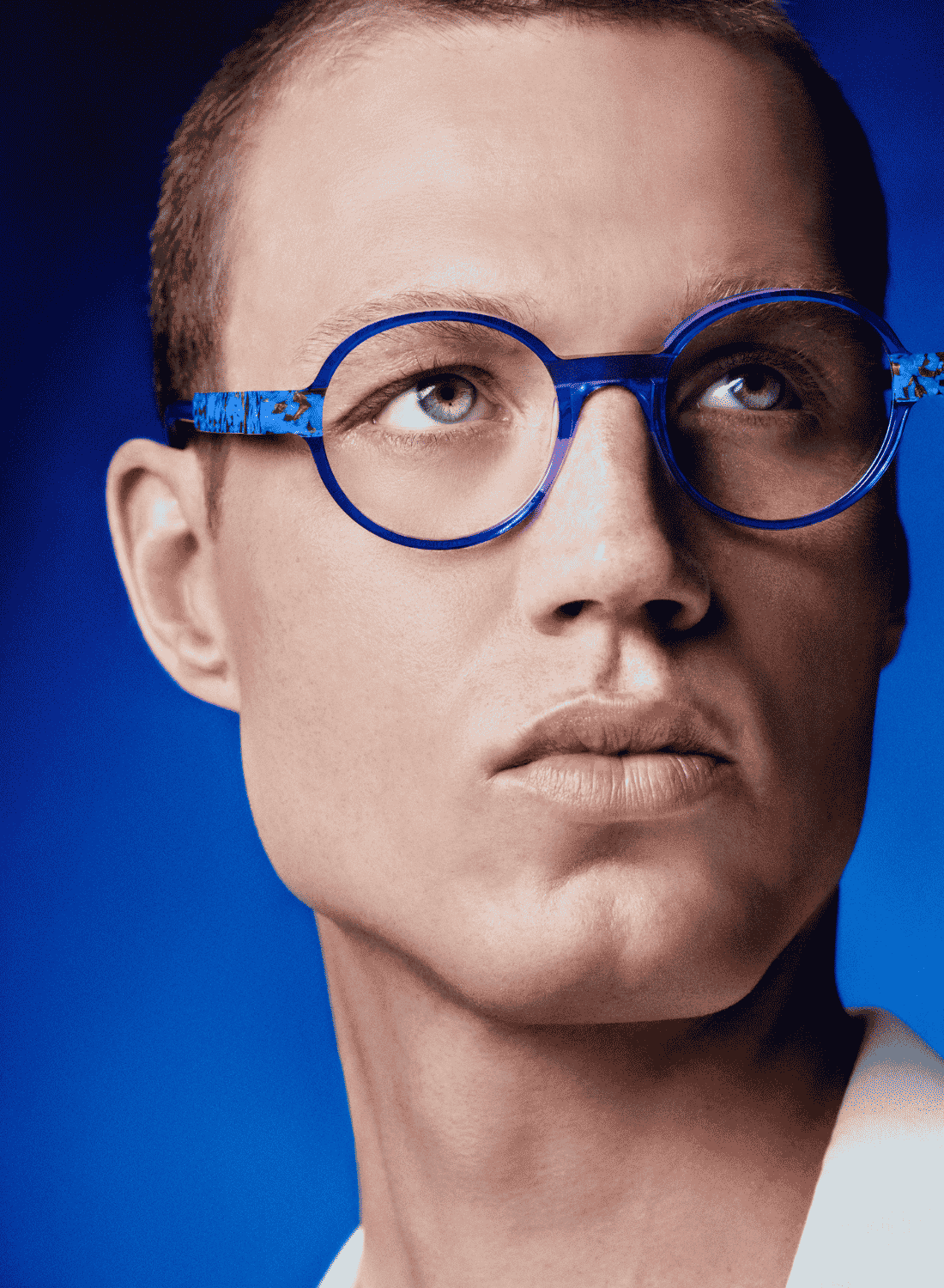 Portrait of a man wearing bright blue round glasses against a blue background