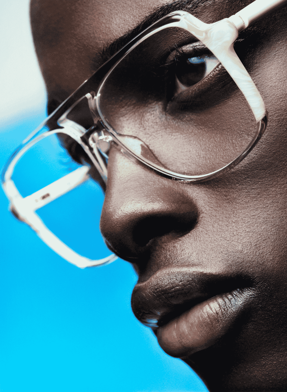 Close-up profile of a person wearing clear eyeglasses against a bright blue background